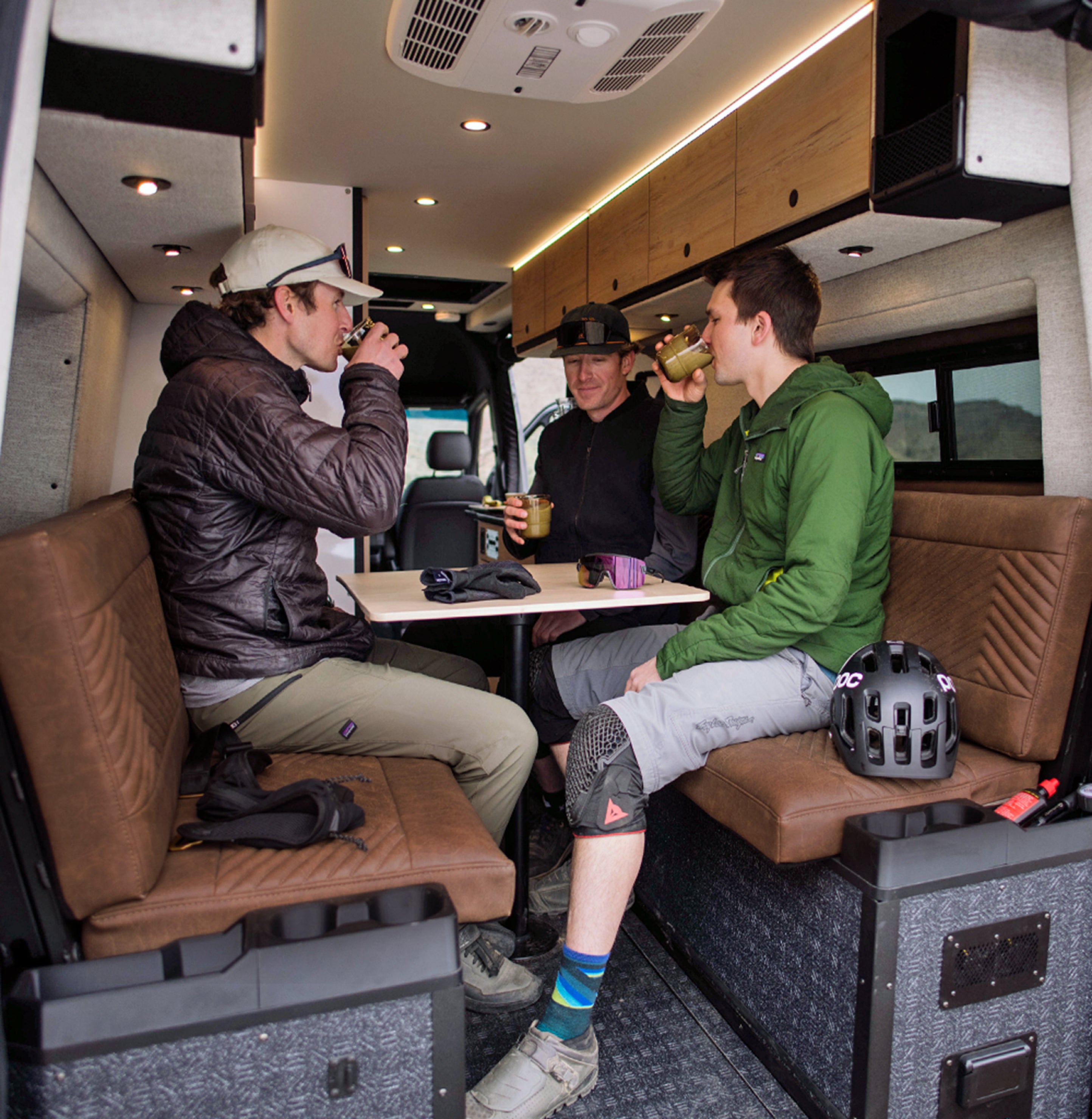 Friends relaxing inside a camper van lounge, enjoying drinks on an adventure van road trip.