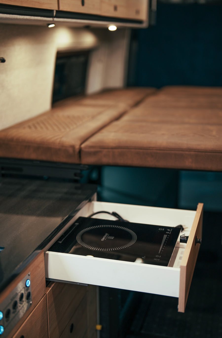 Camper van interior with convertible bed and built-in induction stove, ideal for van life and overlanding.