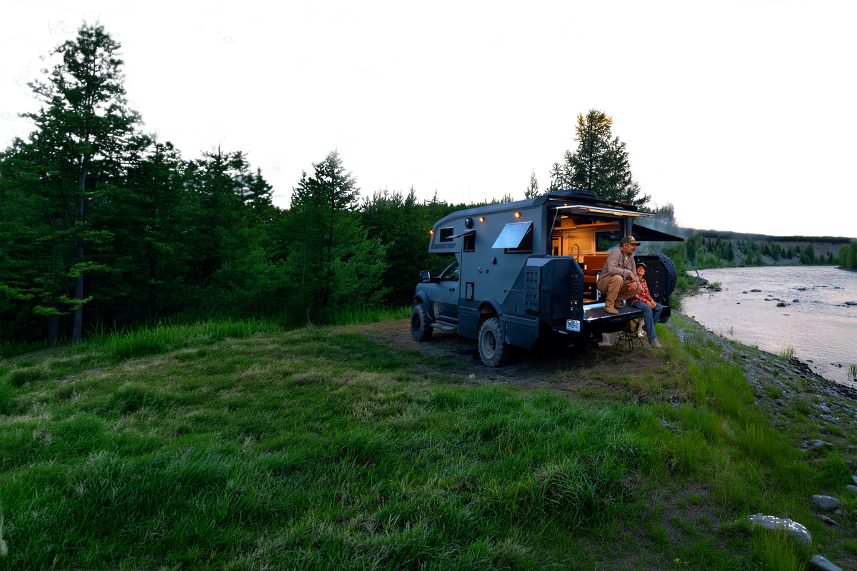 Overlanding adventure van parked by river, couple relaxing at dusk — perfect for vanlife & off-road travel.
