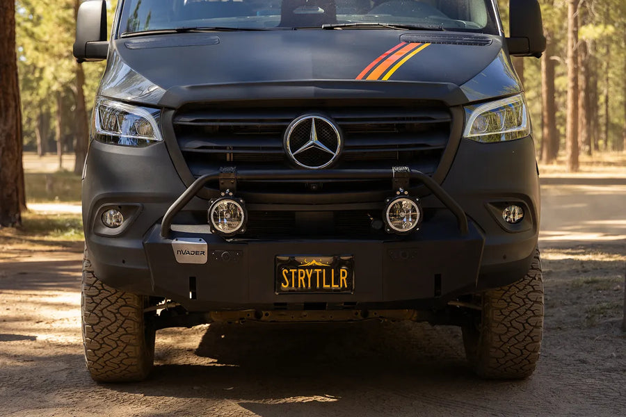 Black 4x4 van with offroad bumper and lights, ready for overlanding adventures in the forest.