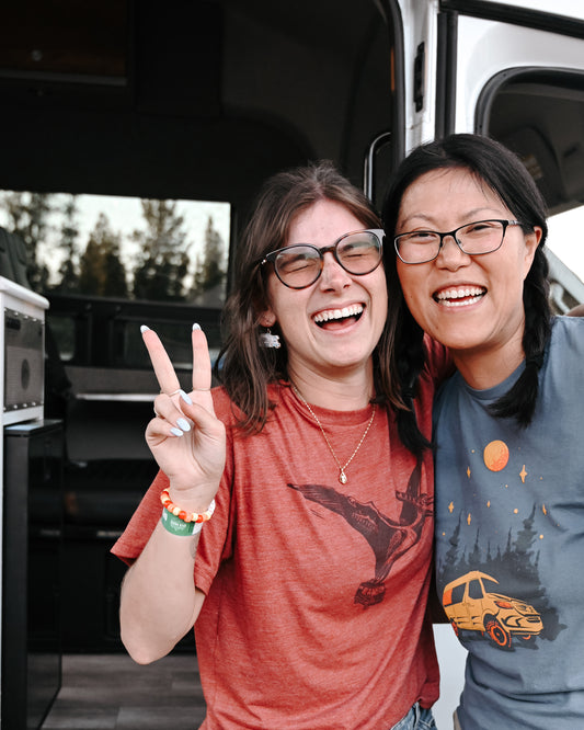 Two women smiling in front of a camper van, enjoying vanlife and adventure travel